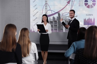 Image of Business trainers giving lecture using video projector in conference room. Building and graphs on projection screen