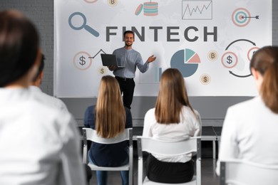 Image of Business trainer giving lecture using video projector in conference room. Fintech word and illustrations on projection screen