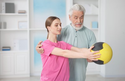 Photo of Doctor and patient exercising with medicine ball in clinic