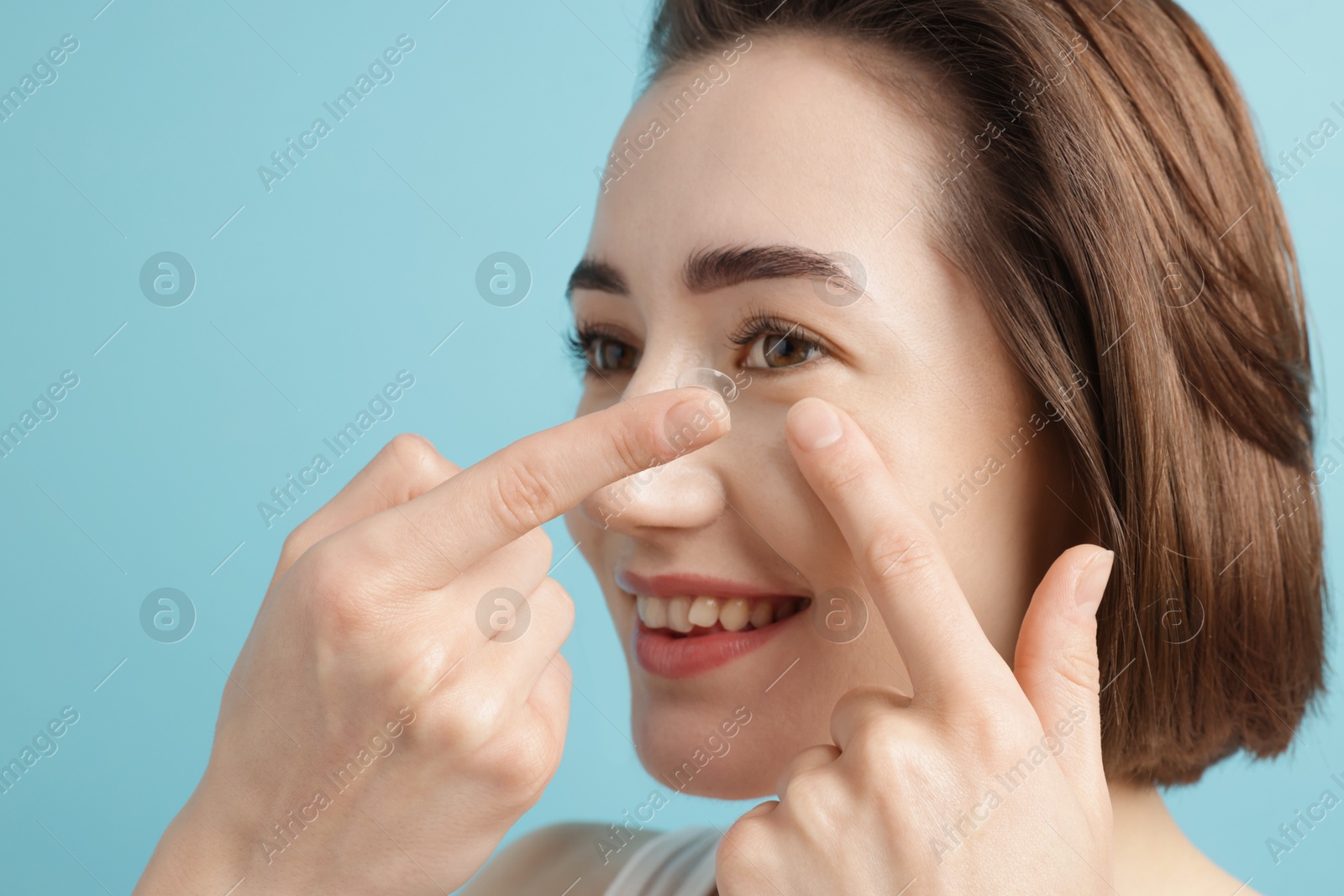 Woman putting in contact lens on light blue background, closeup Photo of Woman putting in contact lens on light blue background, closeup