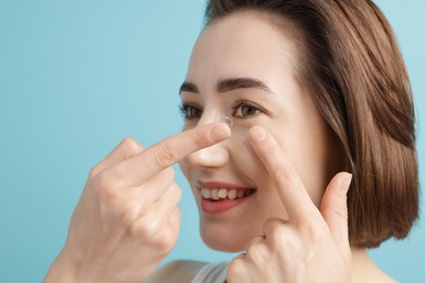 Photo of Woman putting in contact lens on light blue background, closeup