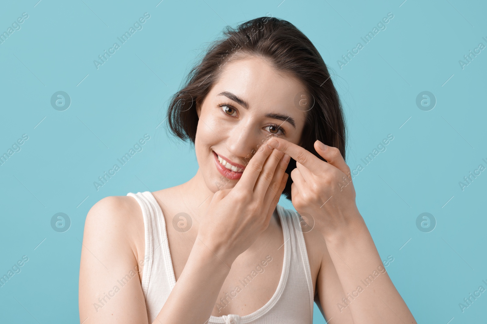 Woman putting in contact lens on light blue background Photo of Woman putting in contact lens on light blue background