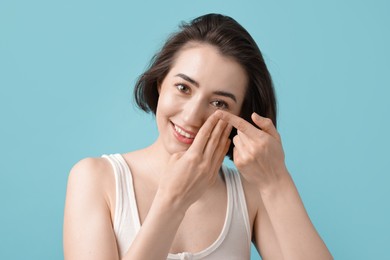 Photo of Woman putting in contact lens on light blue background