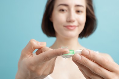 Photo of Woman with contact lens and case on light blue background, selective focus