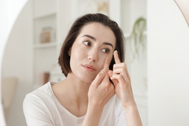 Photo of Woman putting in contact lens near mirror indoors