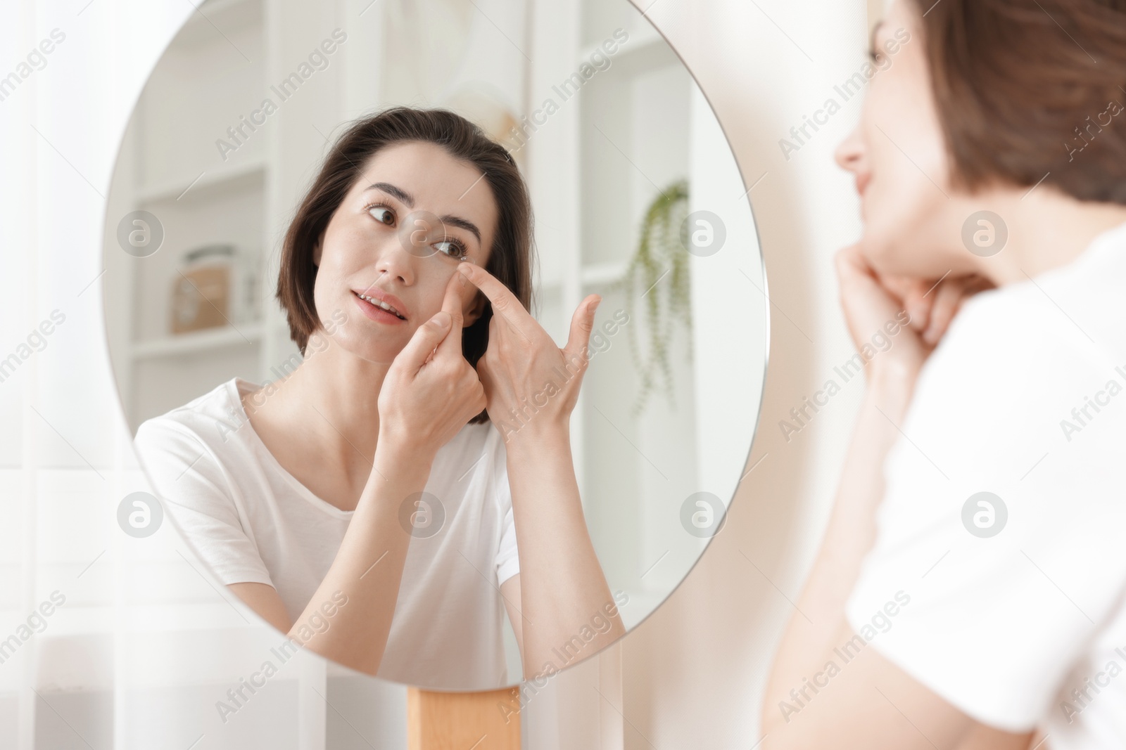Woman putting in contact lens near mirror indoors Photo of Woman putting in contact lens near mirror indoors