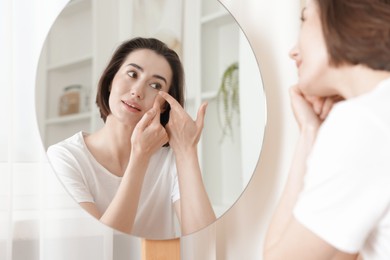 Photo of Woman putting in contact lens near mirror indoors