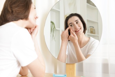 Photo of Woman putting in contact lens near mirror indoors