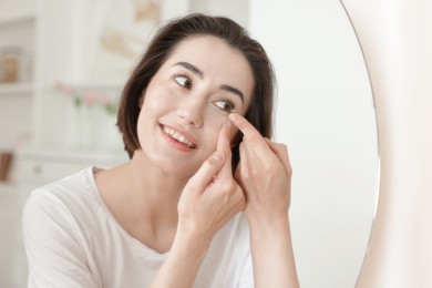 Photo of Woman putting in contact lens near mirror indoors