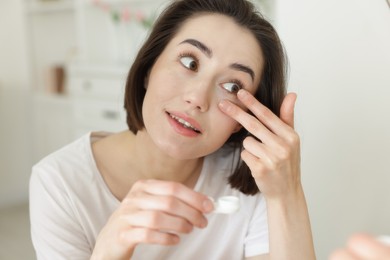Photo of Beautiful woman putting in contact lens indoors