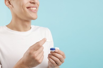 Photo of Man with contact lens and case on light blue background, closeup. Space for text