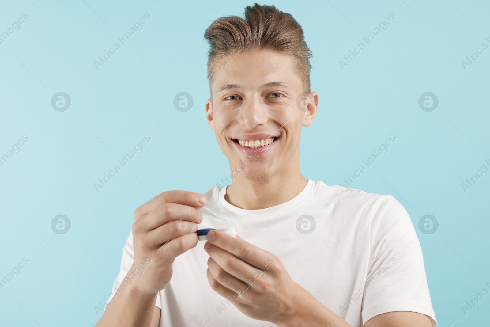Man taking contact lens out of case on light blue background Photo of Man taking contact lens out of case on light blue background