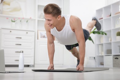 Photo of Man doing plank exercise during online class with coach at home. Sport and healthy lifestyle