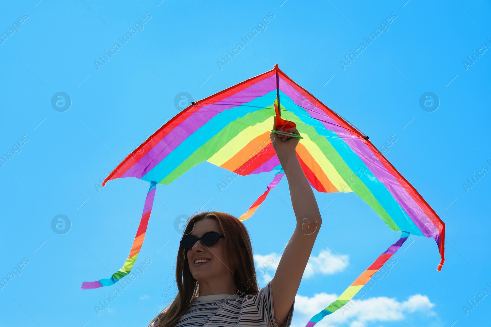 Woman with colorful kite under blue sky, low angle view Photo of Woman with colorful kite under blue sky, low angle view