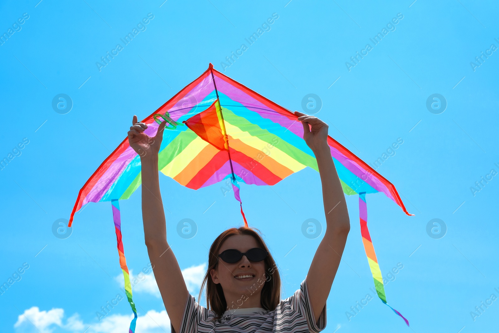 Woman with colorful kite under blue sky, low angle view Photo of Woman with colorful kite under blue sky, low angle view