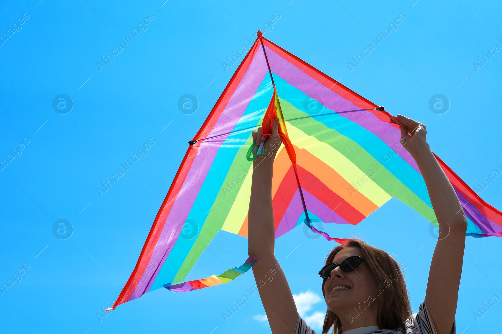 Woman with colorful kite under blue sky, low angle view Photo of Woman with colorful kite under blue sky, low angle view