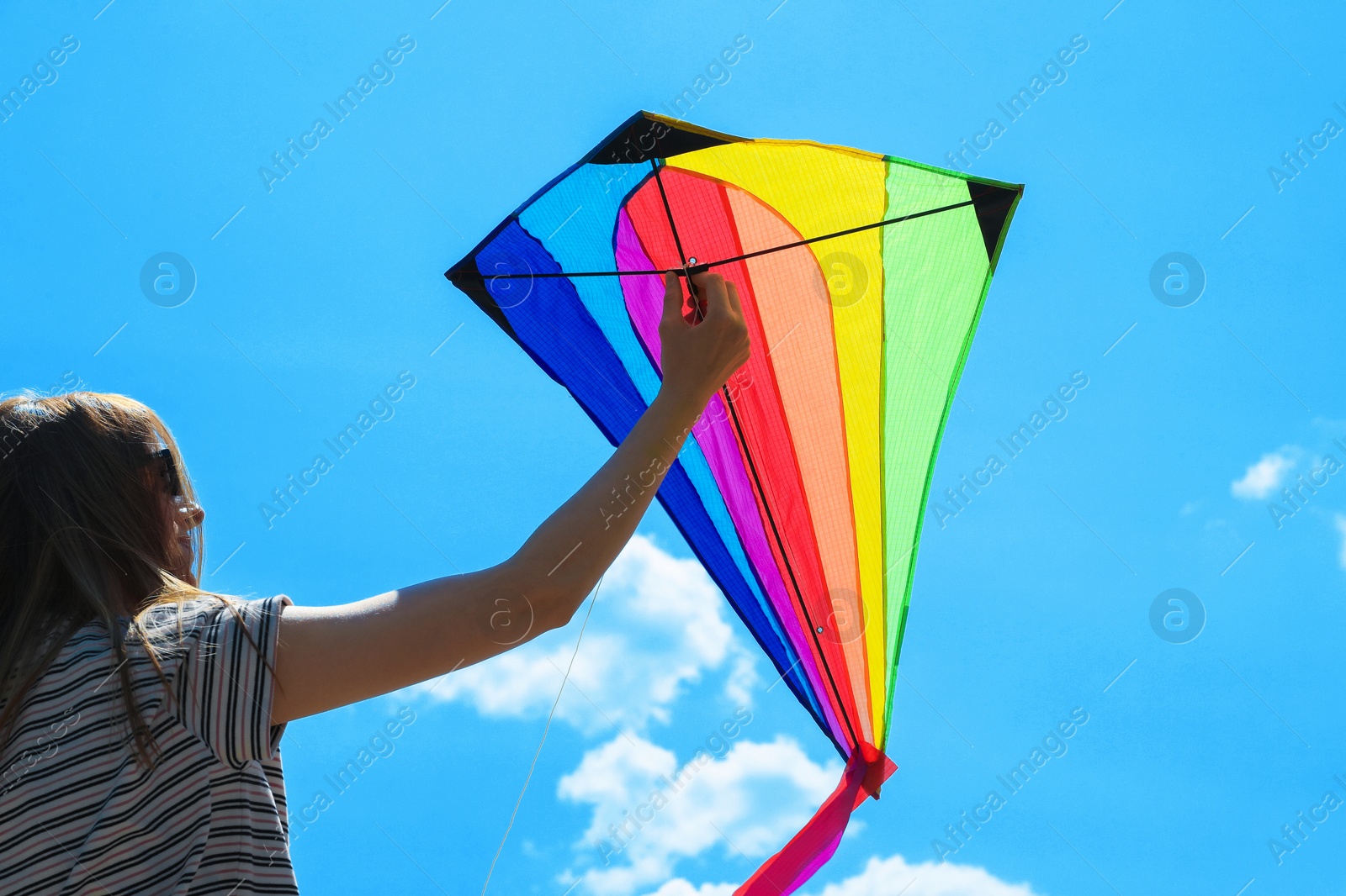 Woman with colorful kite under blue sky, low angle view Photo of Woman with colorful kite under blue sky, low angle view