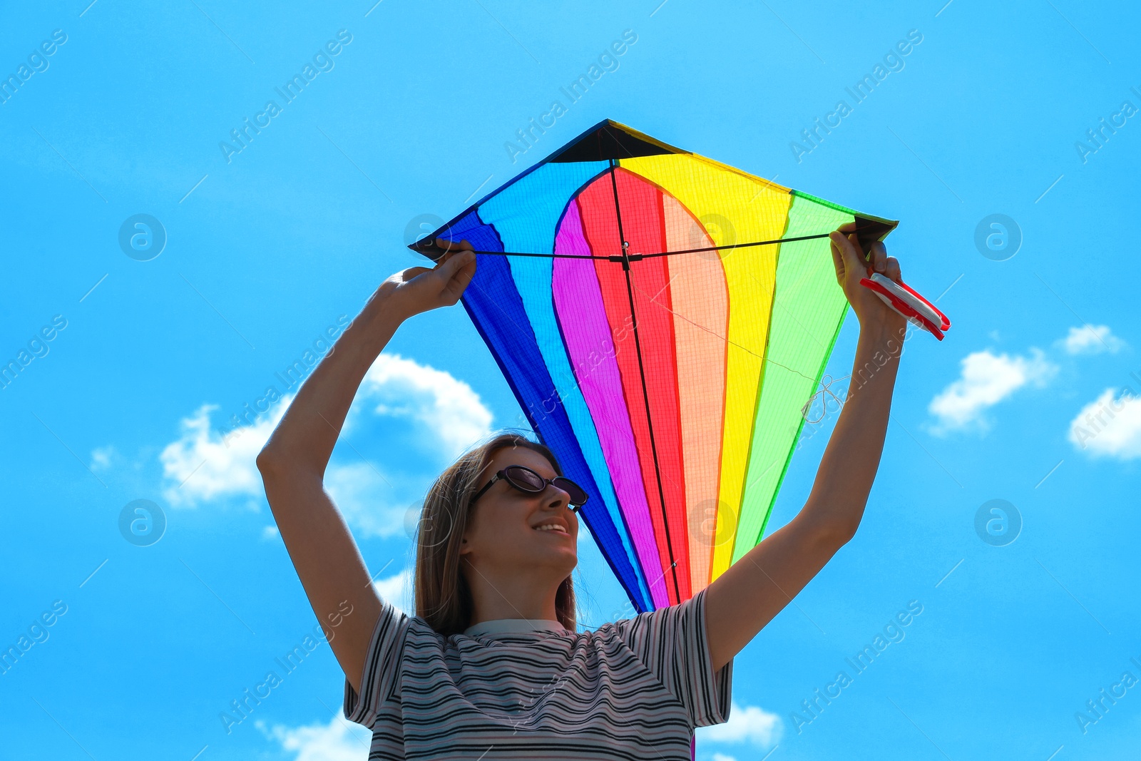 Woman with colorful kite under blue sky, low angle view Photo of Woman with colorful kite under blue sky, low angle view