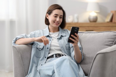 Photo of Woman using modern smartphone in armchair at home