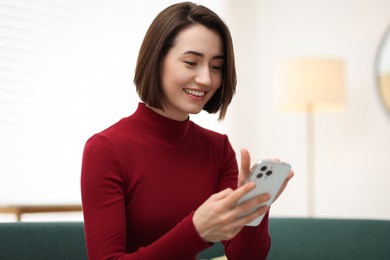 Photo of Woman using modern smartphone on sofa at home