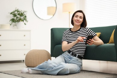 Photo of Woman using modern smartphone on floor at home. Space for text
