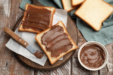 Photo of Sandwiches with chocolate butter and knife on wooden table, flat lay