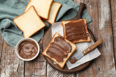 Photo of Sandwiches with chocolate butter and knife on wooden table, flat lay