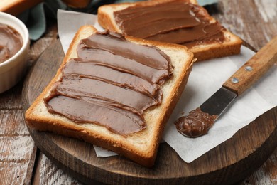 Photo of Sandwiches with chocolate butter and knife on wooden table, closeup