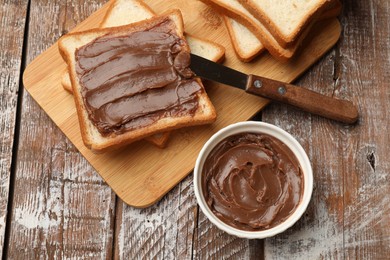Photo of Sandwiches with chocolate butter and knife on wooden table, flat lay