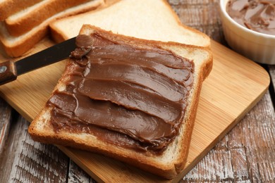 Photo of Sandwiches with chocolate butter and knife on wooden table, closeup