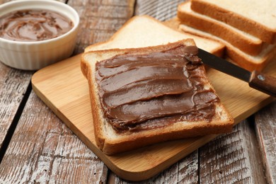 Photo of Sandwiches with chocolate butter and knife on wooden table, closeup