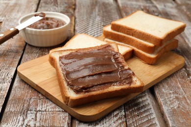 Photo of Sandwiches with chocolate butter and knife on wooden table, closeup