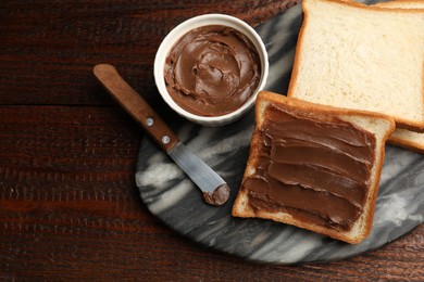 Photo of Sandwiches with chocolate butter and knife on wooden table, flat lay