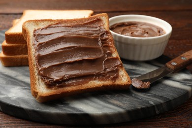 Photo of Sandwiches with chocolate butter and knife on wooden table, closeup