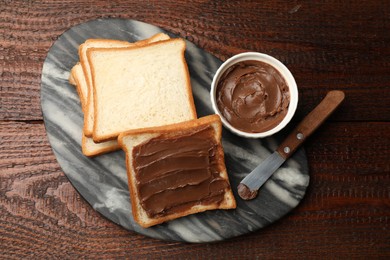 Photo of Sandwiches with chocolate butter and knife on wooden table, flat lay