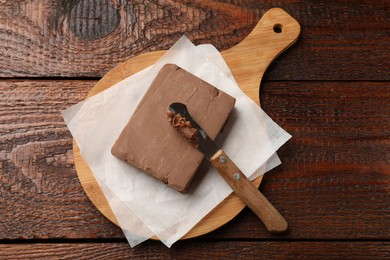 Photo of Block of tasty chocolate butter and knife on wooden table, top view