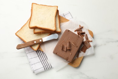Photo of Block of tasty chocolate butter, bread slices and knife on white marble table, top view