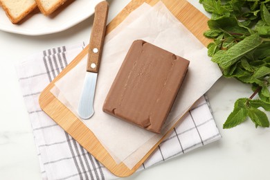 Photo of Block of tasty chocolate butter, knife and bread on white table, flat lay