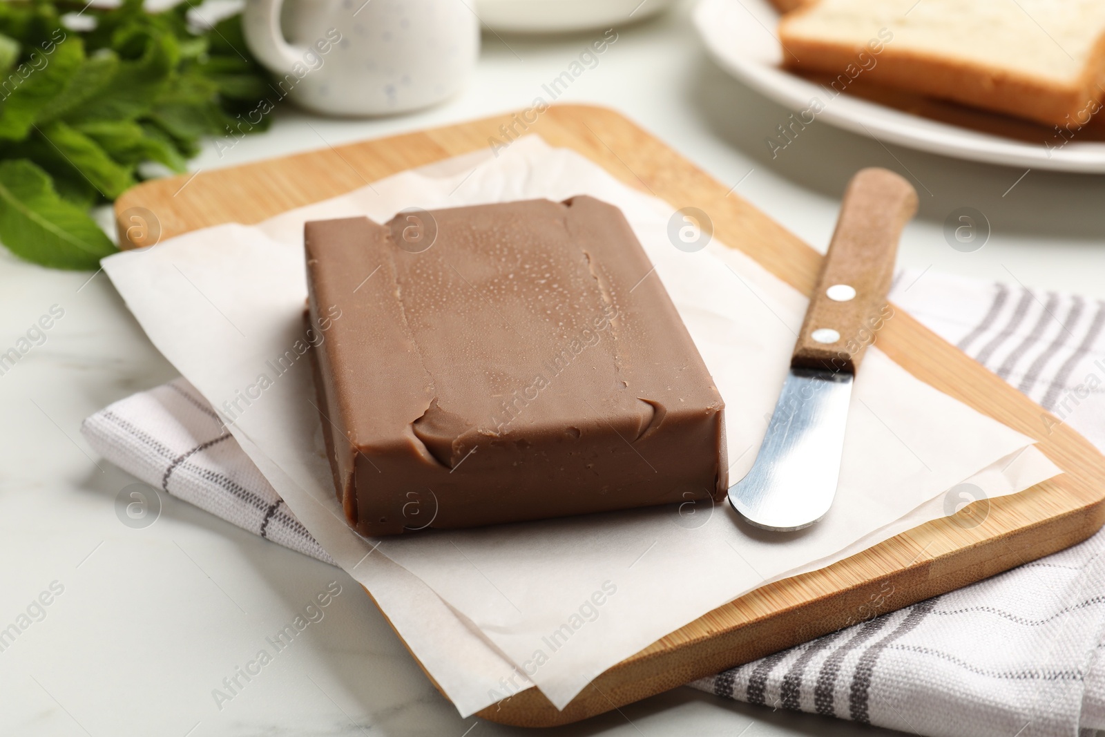 Block of tasty chocolate butter and knife on light table, closeup Photo of Block of tasty chocolate butter and knife on light table, closeup