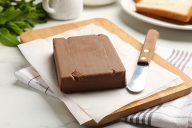 Photo of Block of tasty chocolate butter and knife on light table, closeup