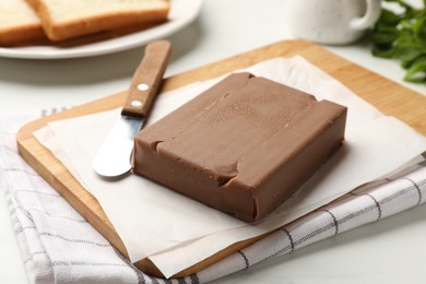 Photo of Block of tasty chocolate butter and knife on light table, closeup