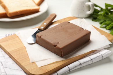 Photo of Block of tasty chocolate butter and knife on light table, closeup