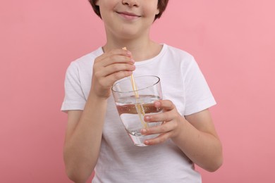 Photo of Little boy with glass of refreshing soda drink on pink background, closeup
