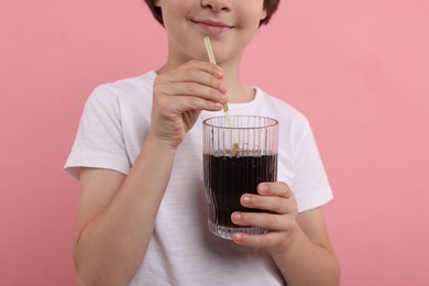Photo of Little boy with glass of refreshing soda drink on pink background, closeup