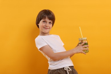 Photo of Cute little boy with mason jar of lemonade on orange background. Refreshing drink