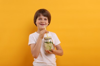 Photo of Cute little boy with mason jar of lemonade on orange background. Refreshing drink