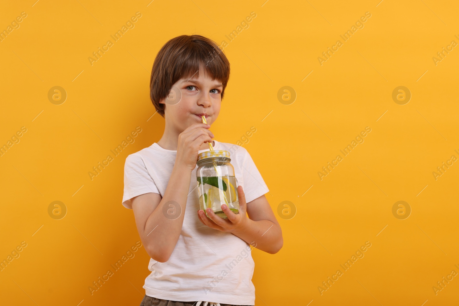 Cute little boy drinking lemonade on orange background. Refreshing drink Photo of Cute little boy drinking lemonade on orange background. Refreshing drink