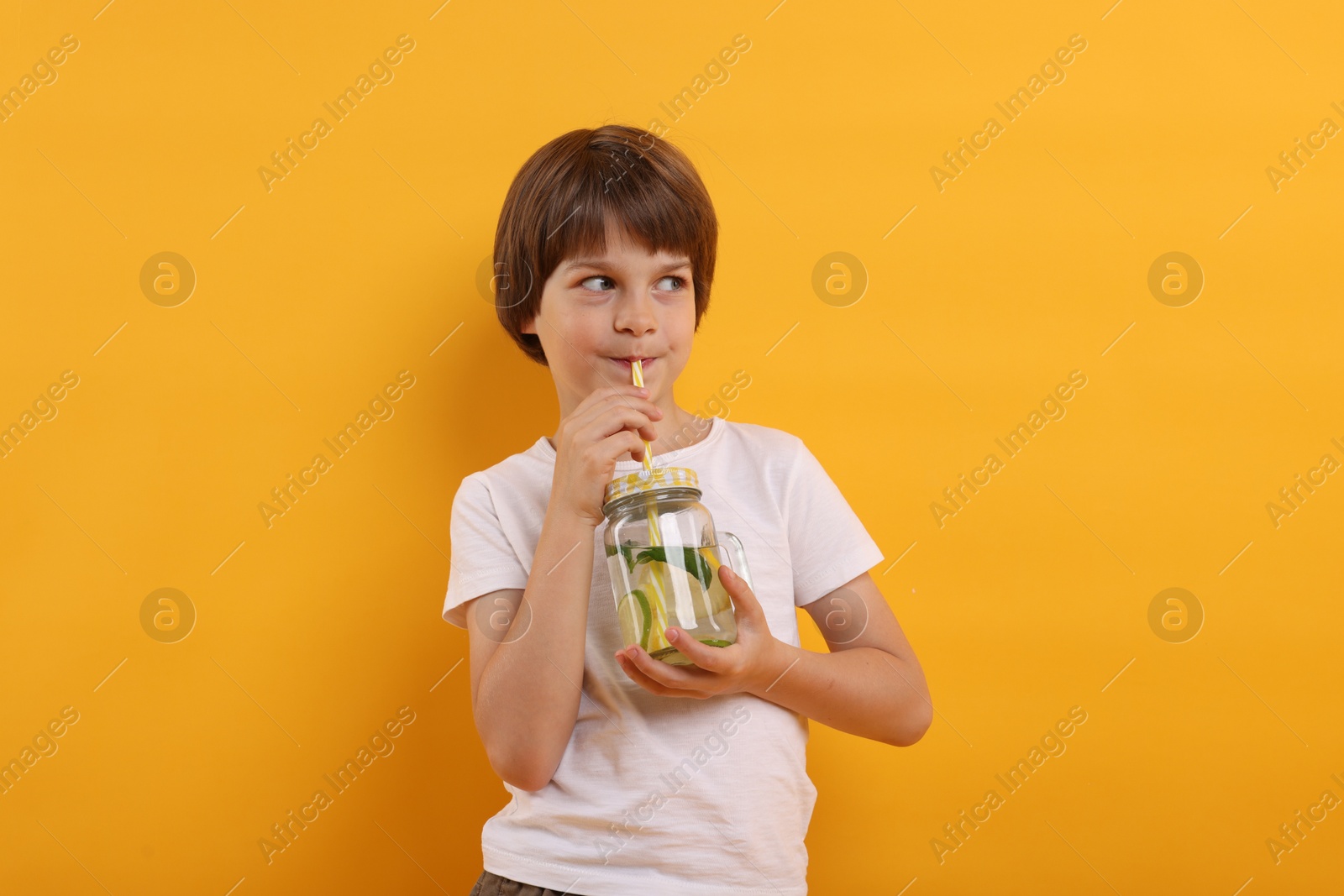 Cute little boy drinking lemonade on orange background. Refreshing drink Photo of Cute little boy drinking lemonade on orange background. Refreshing drink