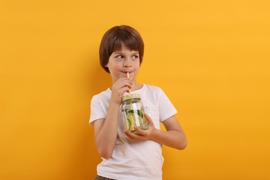 Photo of Cute little boy drinking lemonade on orange background. Refreshing drink