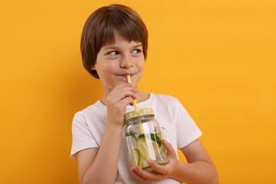 Photo of Cute little boy drinking lemonade on orange background. Refreshing drink